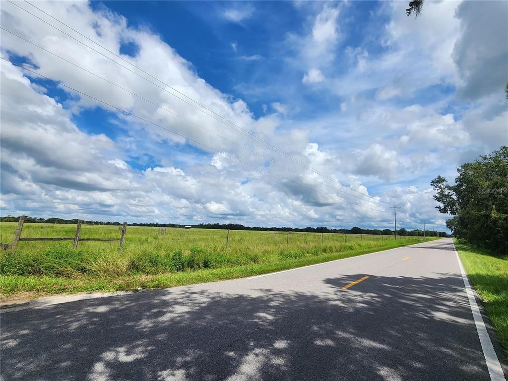 A paved road runs alongside a large, grassy field bordered by a wooden fence — GOUGH ROAD, ONA, FL