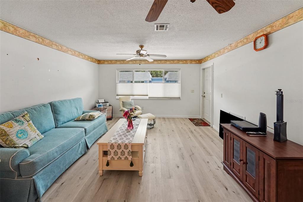 A living room features light wood-look flooring, a blue sofa, a coffee table, and a ceiling fan — 6880 LAFAYETTE N UNIT 8, PINELLAS PARK, FL