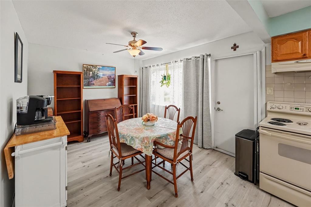 A dining area with wood-look flooring, a round table, and a kitchen to the right — 6880 LAFAYETTE N UNIT 8, PINELLAS PARK, FL
