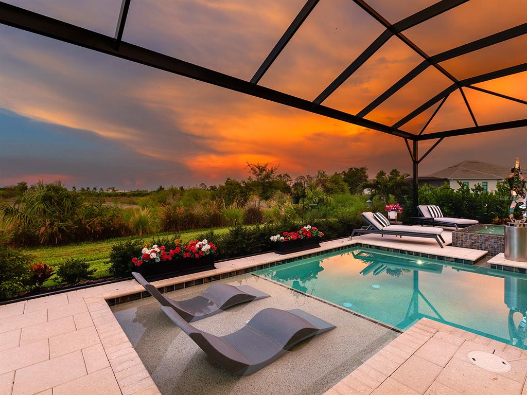 A swimming pool with lounge chairs sits under a screened enclosure at sunset — 1095 BLUE SHELL LOOP, SARASOTA, FL