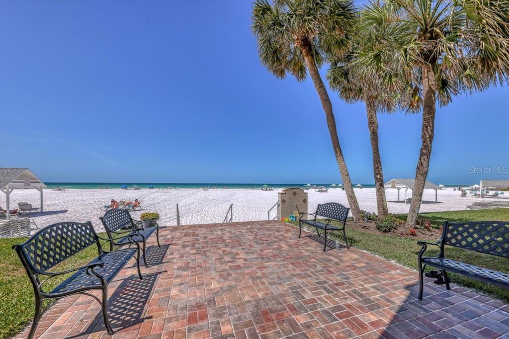 A brick patio with three metal benches overlooks a white sand beach and ocean — 6154 MIDNIGHT PASS ROAD UNIT C08, SARASOTA, FL