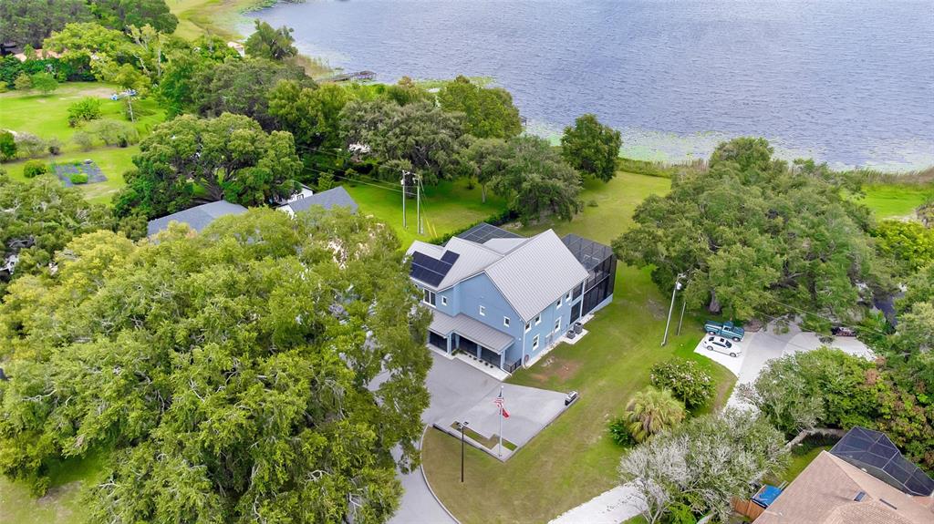An aerial view shows a blue two-story house with solar panels near a lake — 1317 SPRING LAKE TERRACE, OCOEE, FL
