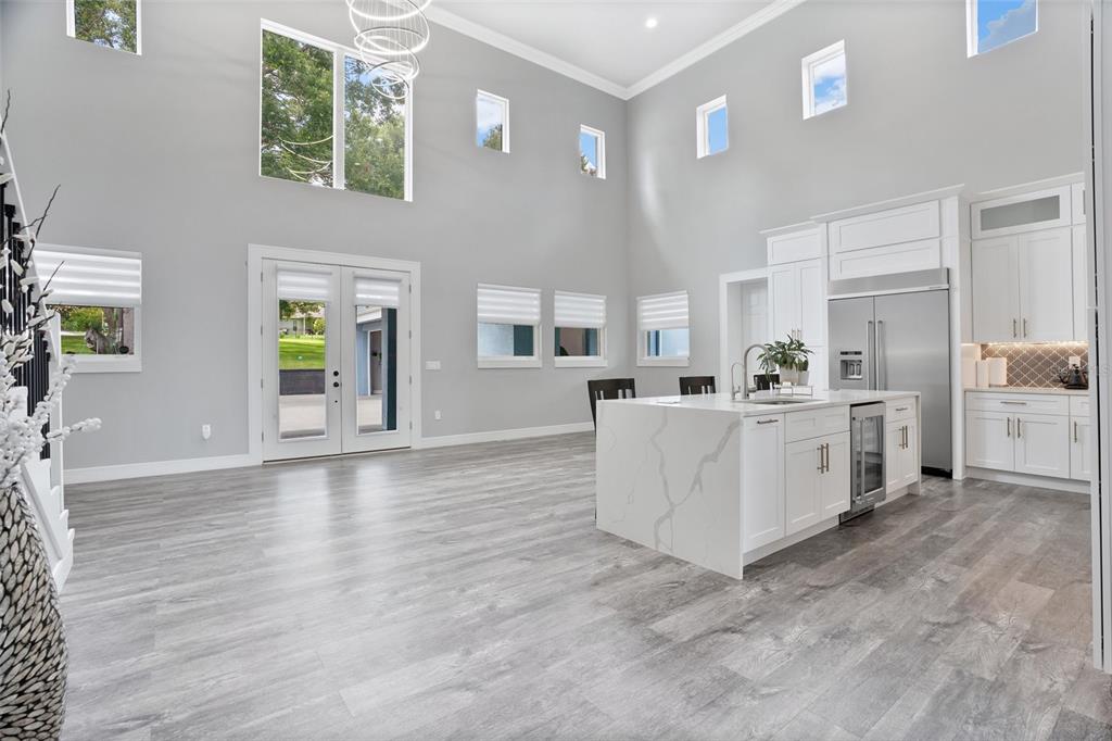 A modern, open-concept kitchen and living area features high ceilings, white cabinetry, and gray flooring — 1317 SPRING LAKE TERRACE, OCOEE, FL