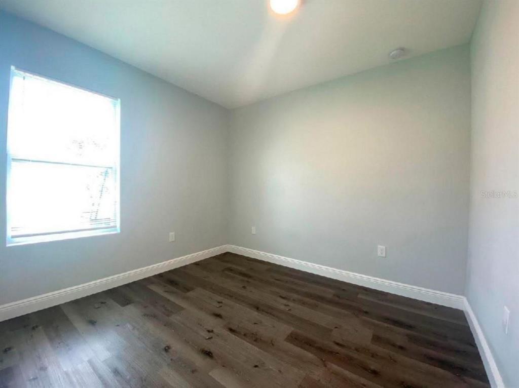 An empty room features light gray walls, white trim, and dark wood-look flooring — 1813 PUFFIN STREET UNIT 1813, SEBRING, FL
