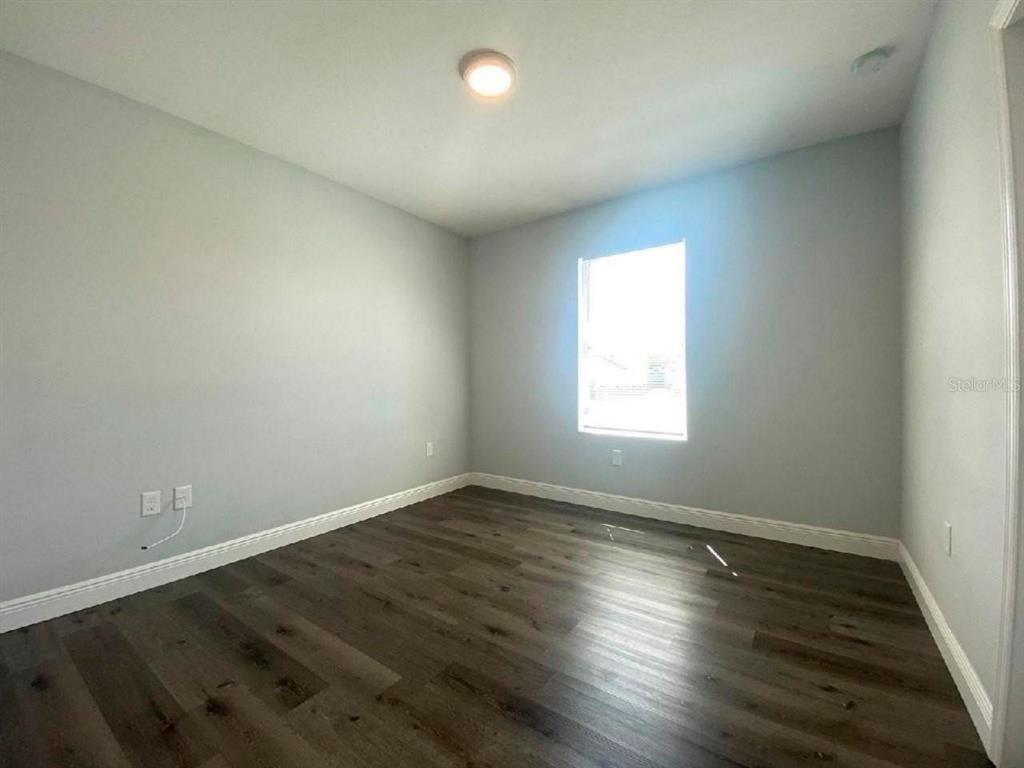 An empty bedroom features light gray walls, dark wood-look flooring, and a single window — 1813 PUFFIN STREET UNIT 1813, SEBRING, FL