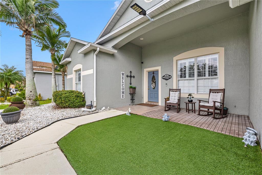 A house exterior features a front porch with two rocking chairs, artificial turf, and landscaping — 255 STRATHMORE CIRCLE, KISSIMMEE, FL