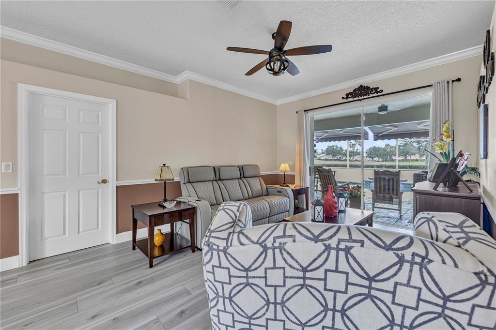 A living room features a gray sofa, patterned armchair, wood-look flooring, and sliding glass doors — 255 STRATHMORE CIRCLE, KISSIMMEE, FL