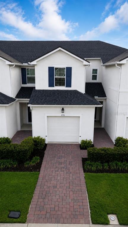 A two-story townhouse exterior features a white facade, dark shutters, and a brick paver driveway — 1190 SEASIDE MIST TRAIL, KISSIMMEE, FL