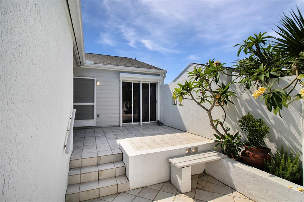 A tiled patio features a small set of stairs, a built-in bench, and a plumeria tree — 971 WATERSIDE LANE, BRADENTON, FL