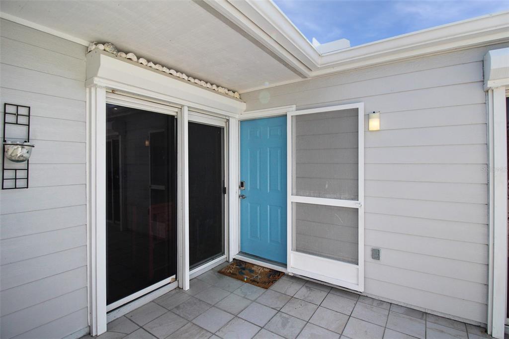 A light blue front door with a screen door sits on a tiled patio — 971 WATERSIDE LANE, BRADENTON, FL