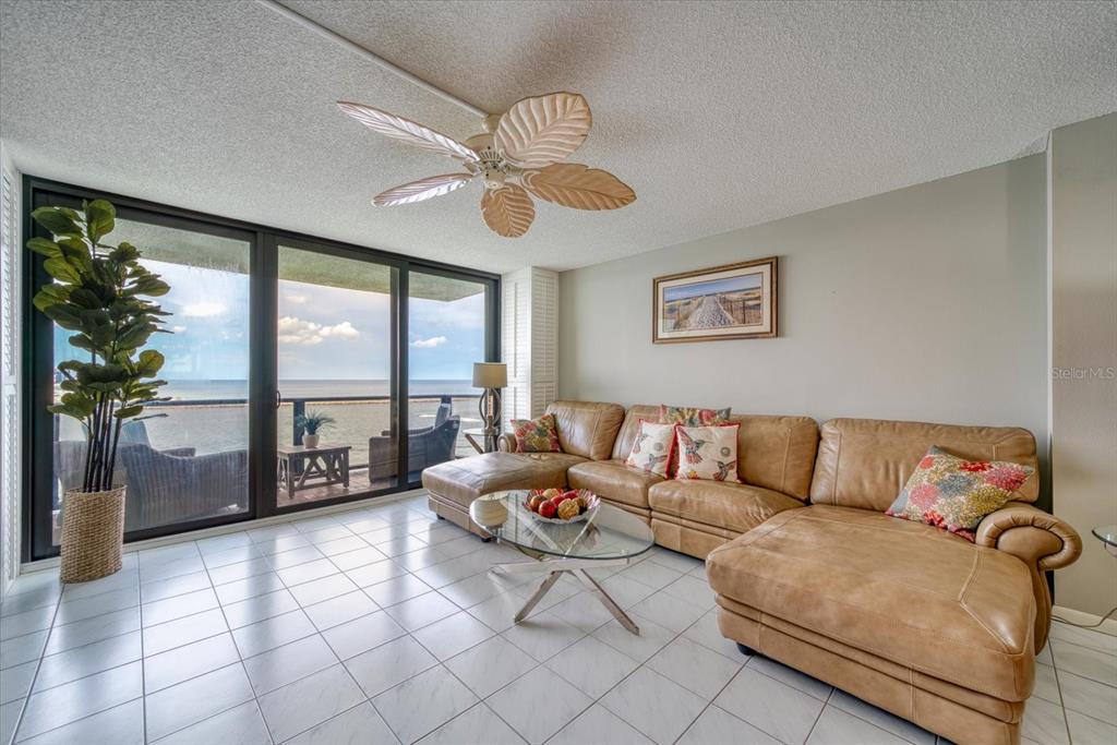 A living room features a tan sectional sofa, glass coffee table, and oceanfront balcony access — 450 S GULFVIEW BOULEVARD UNIT 907, CLEARWATER, FL