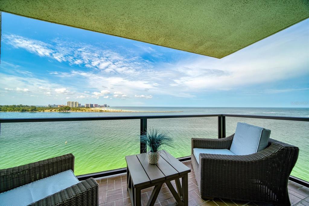 A balcony with two wicker chairs and a small table overlooks the ocean and beach — 450 S GULFVIEW BOULEVARD UNIT 907, CLEARWATER, FL