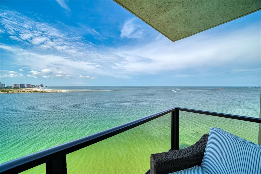 A balcony with a black railing and a wicker chair overlooks the ocean and beach — 450 S GULFVIEW BOULEVARD UNIT 907, CLEARWATER, FL
