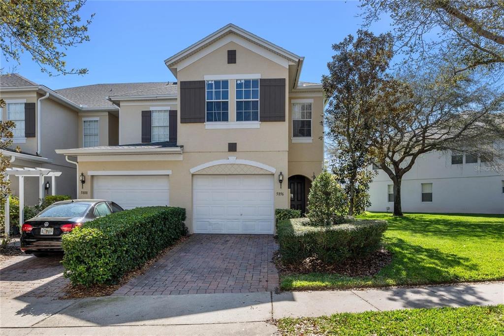 A two-story beige townhouse features a brick driveway, a white garage door, and manicured hedges — 5896 STRADA CAPRI WAY, ORLANDO, FL