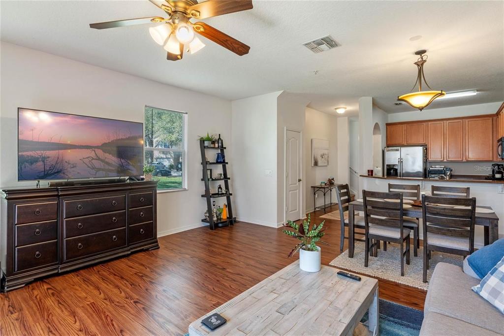 A living room with wood-look flooring, a ceiling fan, a television, and an adjacent dining area — 5896 STRADA CAPRI WAY, ORLANDO, FL