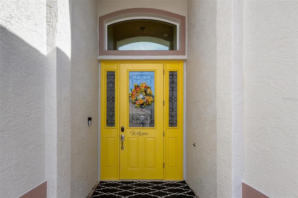 A bright yellow front door with a glass insert and sidelights sits under an arched transom — 26238 FEATHERSOUND DRIVE, PUNTA GORDA, FL
