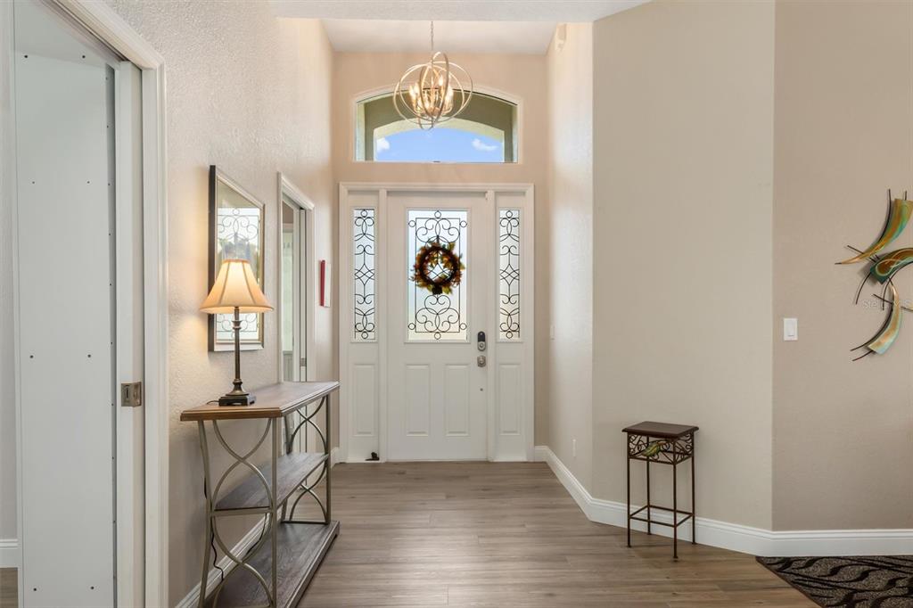 A bright entryway features a white front door with glass panels, wood flooring, and lighting — 26238 FEATHERSOUND DRIVE, PUNTA GORDA, FL