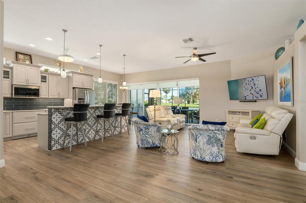 An open-concept kitchen and living area featuring light wood flooring, bar seating, and patio views — 26238 FEATHERSOUND DRIVE, PUNTA GORDA, FL