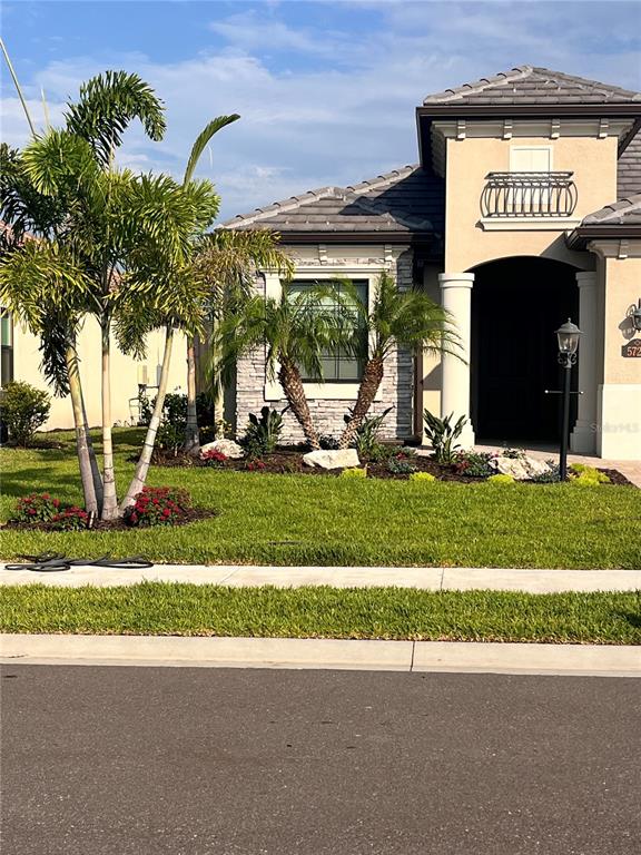 A single-story house with a stone facade, palm trees, and a dark arched entryway — 5720 CHEECH GLEN, BRADENTON, FL