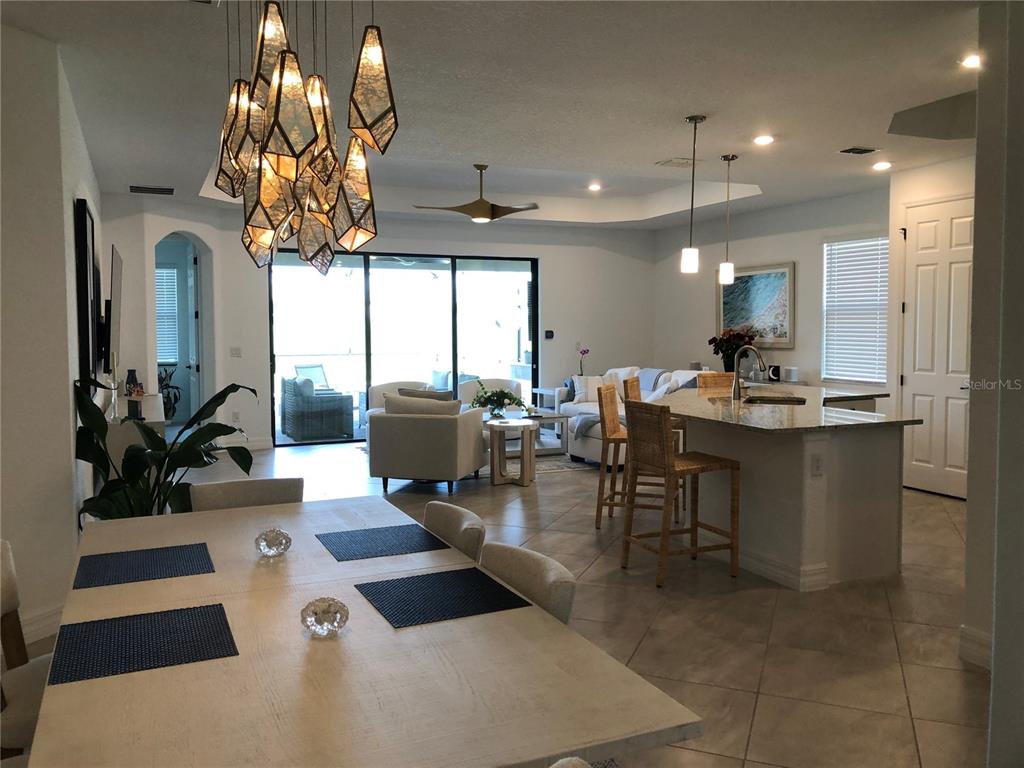 An open-concept living area features a dining table, kitchen island with barstools, and sliding doors — 5720 CHEECH GLEN, BRADENTON, FL