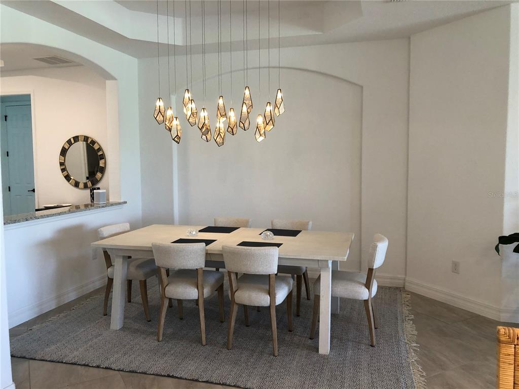 A dining room features a light-colored table, six chairs, a textured rug, and geometric pendant lights — 5720 CHEECH GLEN, BRADENTON, FL
