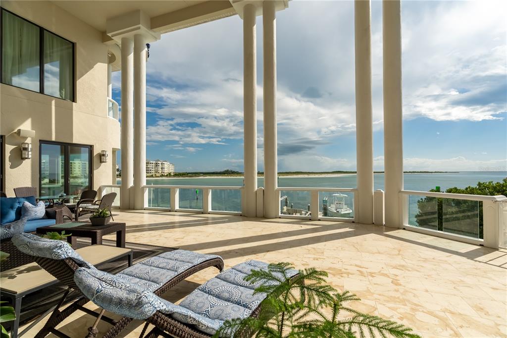 A spacious covered patio features wicker furniture, stone flooring, and expansive views of the ocean — 774 NINA DRIVE, TIERRA VERDE, FL