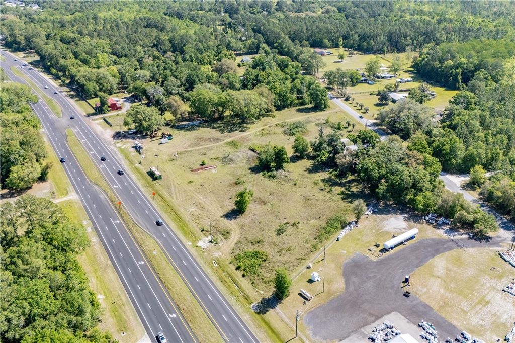 An aerial view shows a multi-lane highway bordering a large, undeveloped grassy lot with trees — 9627 US HIGHWAY 301 HIGHWAY N, HAMPTON, FL