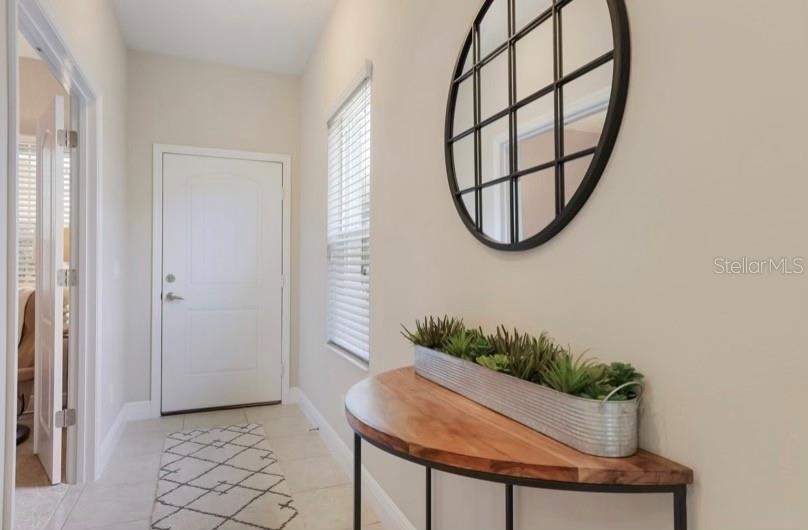 A bright entryway features a white door, tile flooring, a half-moon console table, and wall mirror — 13012 DEEP BLUE PLACE, BRADENTON, FL