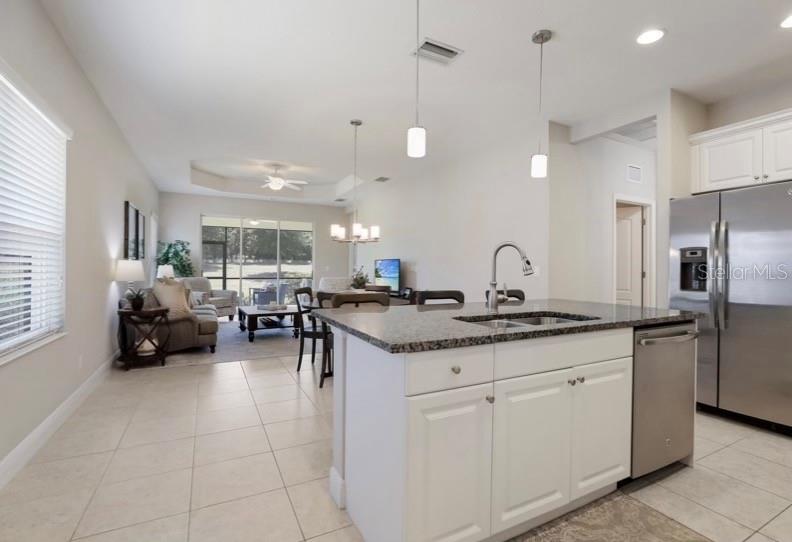 A kitchen island with a granite countertop sits in front of an open-concept living area — 13012 DEEP BLUE PLACE, BRADENTON, FL