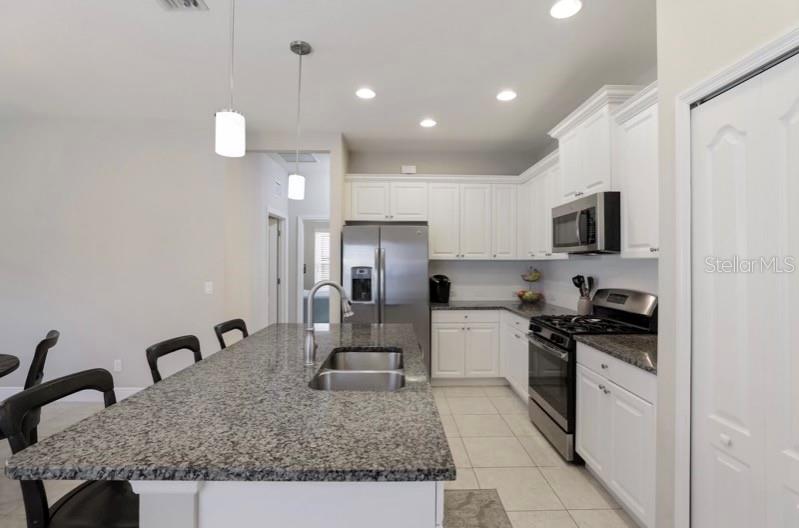 A kitchen features a granite-topped island, white cabinetry, stainless steel appliances, and tile flooring — 13012 DEEP BLUE PLACE, BRADENTON, FL