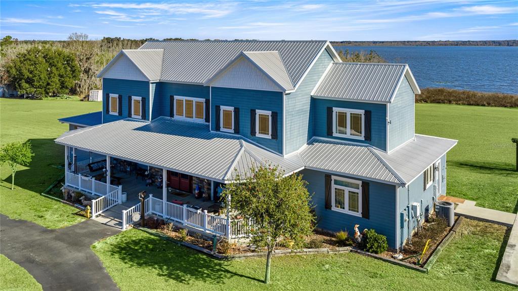 A two-story blue house with a metal roof and a wrap-around porch overlooks a lake — 5251 SE 180TH AVENUE ROAD, OCKLAWAHA, FL