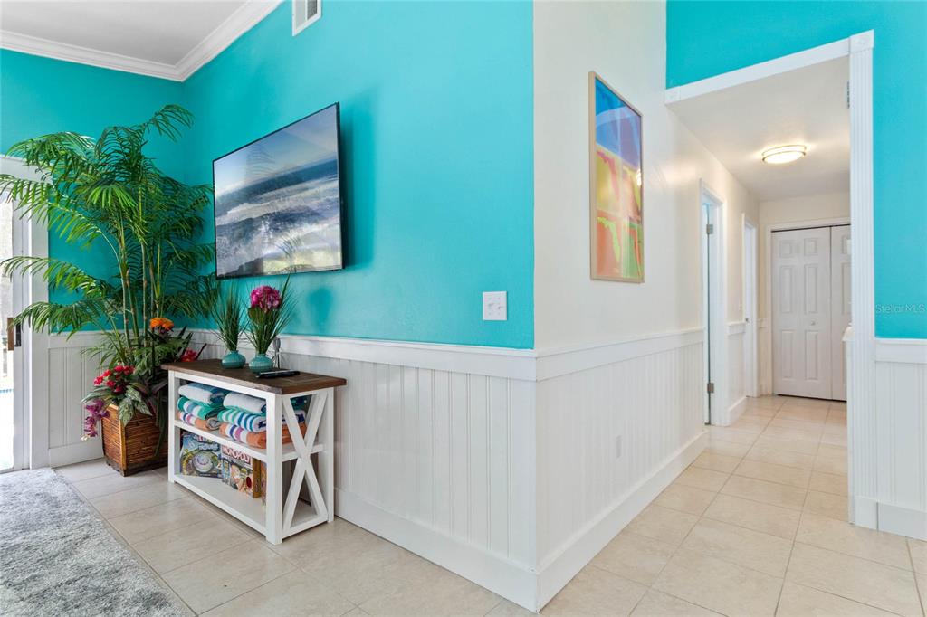 A bright turquoise hallway features white wainscoting, a wall-mounted television, and a console table — 125 HIDDEN SPRINGS CIRCLE, KISSIMMEE, FL