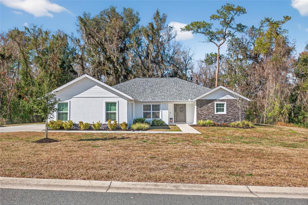 A single-story house with white stucco siding, a stone accent wall, and a gray roof — 10160 SE 41ST AVENUE, BELLEVIEW, FL