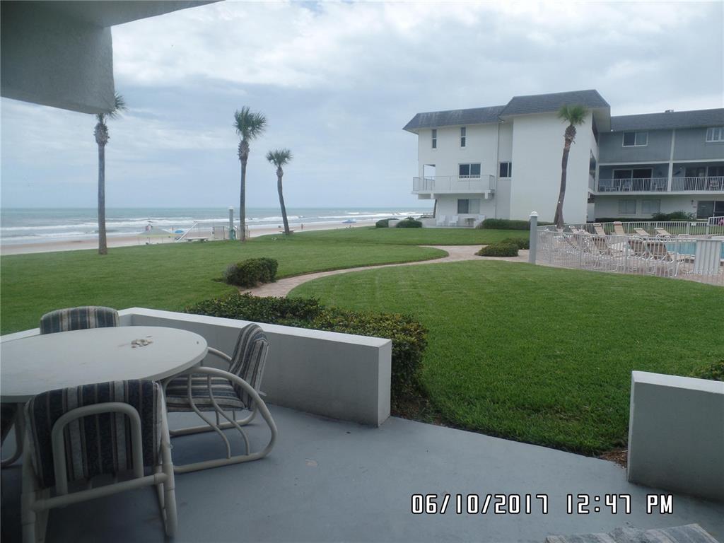 A patio with a table and chairs overlooks a grassy lawn, palm trees, and the ocean — 815 OCEAN SHORE BOULEVARD UNIT 11, ORMOND BEACH, FL