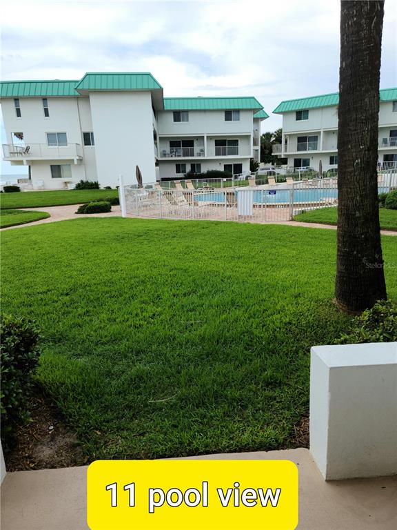 A view of a swimming pool and lawn from a ground-level patio — 815 OCEAN SHORE BOULEVARD UNIT 11, ORMOND BEACH, FL