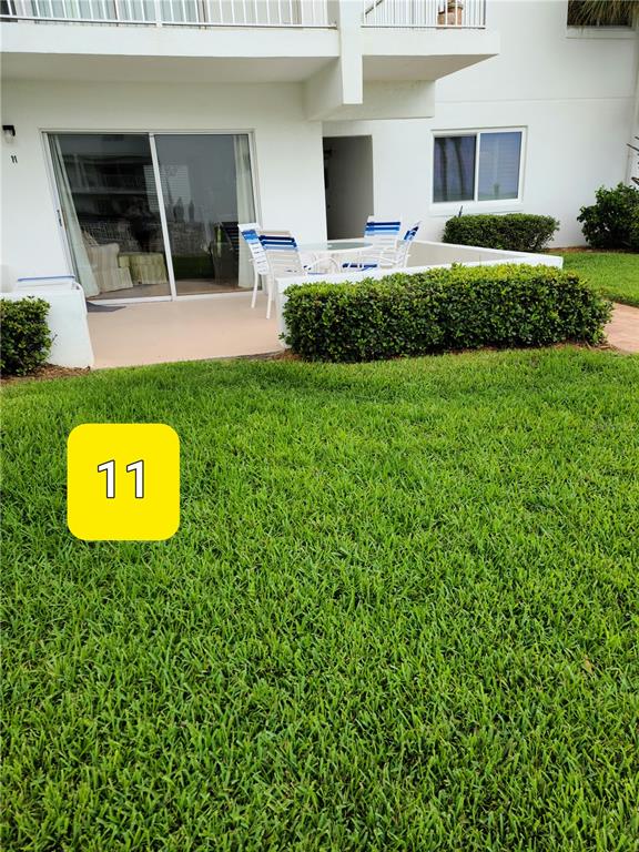 A ground-floor patio with outdoor furniture sits adjacent to a manicured lawn and hedge — 815 OCEAN SHORE BOULEVARD UNIT 11, ORMOND BEACH, FL