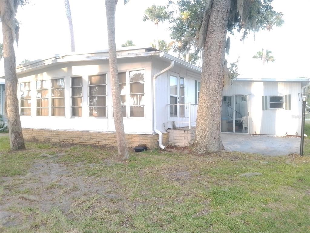 A white mobile home with a brick base, multiple windows, and large trees in front — 112 PALM DRIVE UNIT B, EUSTIS, FL