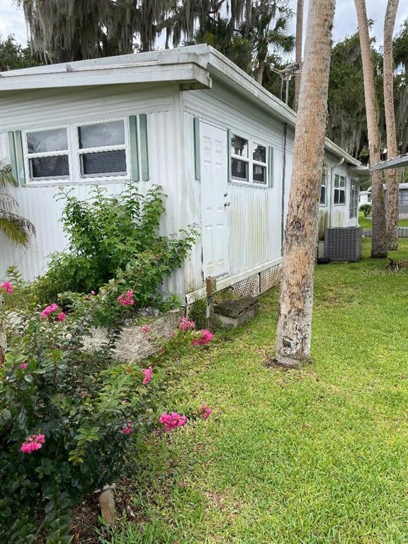 The exterior of a white mobile home features a side door, windows, and landscaping — 112 PALM DRIVE UNIT B, EUSTIS, FL