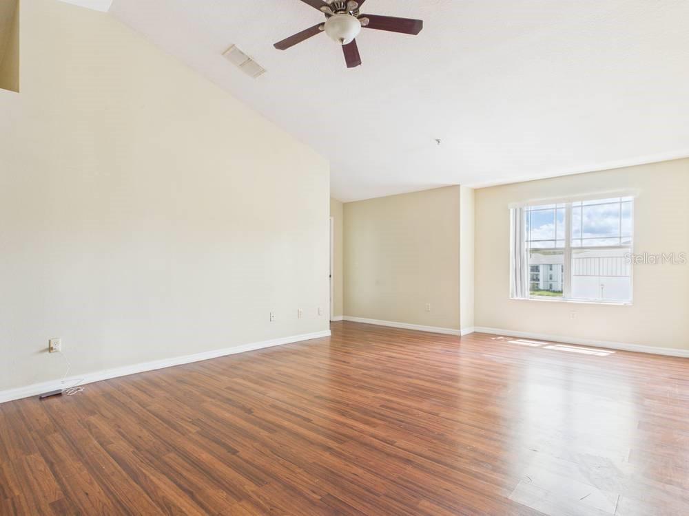 An empty living room features wood-look flooring, a vaulted ceiling with a fan, and a window — 16337 ENCLAVE VILLAGE DRIVE UNIT 16337, TAMPA, FL