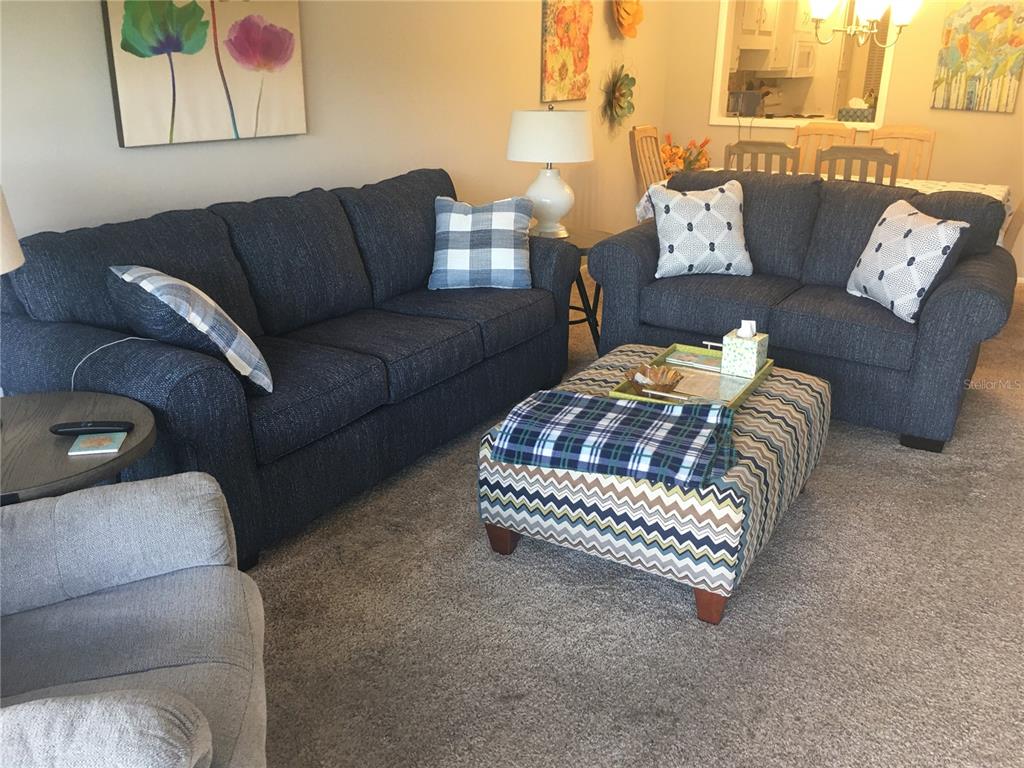 A living room features two dark blue sofas, a patterned ottoman, and a grey armchair — 7405 W COUNTRY CLUB DRIVE N UNIT 104, SARASOTA, FL
