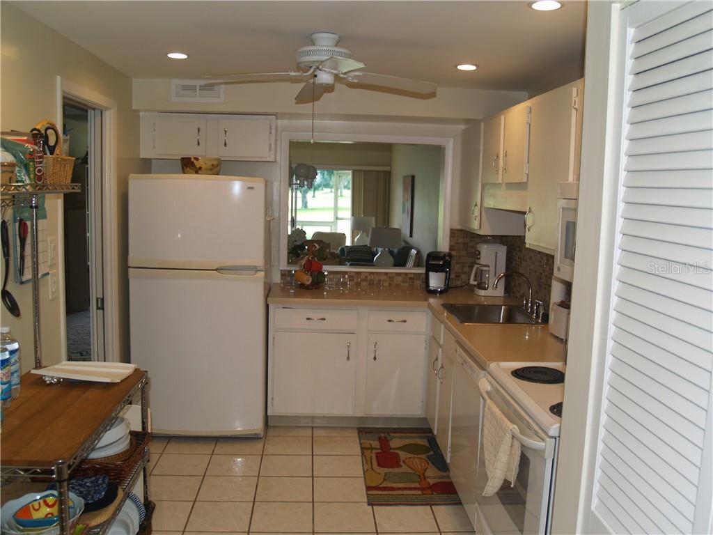 A kitchen with white cabinets, a white refrigerator, a tiled floor, and a pass-through window — 7405 W COUNTRY CLUB DRIVE N UNIT 104, SARASOTA, FL
