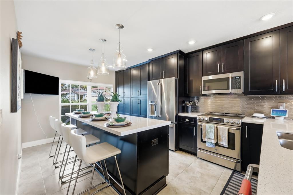 A kitchen with dark cabinets, stainless steel appliances, and a quartz-topped island with a sink — 2909 SOMERSWORTH COURT, ORLANDO, FL