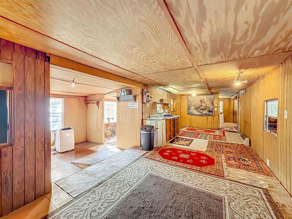 A rustic room features wood-paneled walls, plywood ceilings, and multiple area rugs on the floor — 3180 E BUFFALO LANE, HERNANDO, FL