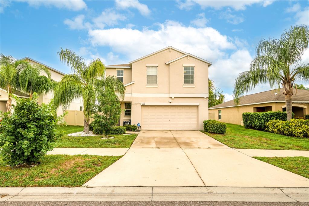 A two-story suburban house with a beige stucco exterior and a two-car garage — 409 SERENITY MILL LOOP, RUSKIN, FL