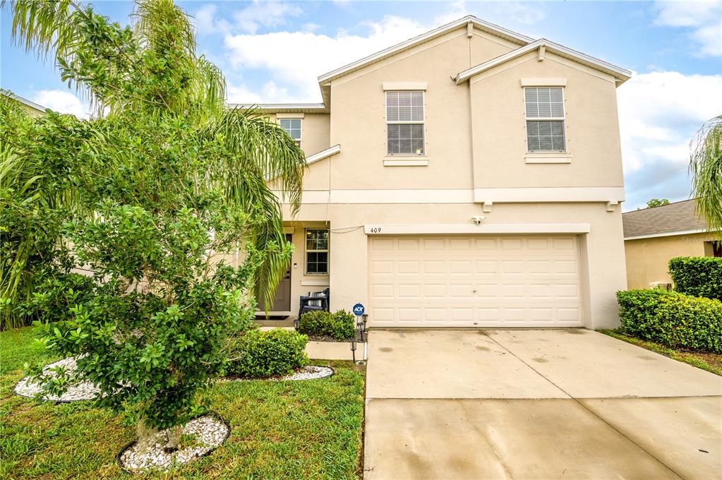 A two-story beige house with a two-car garage and a front yard with palm trees — 409 SERENITY MILL LOOP, RUSKIN, FL