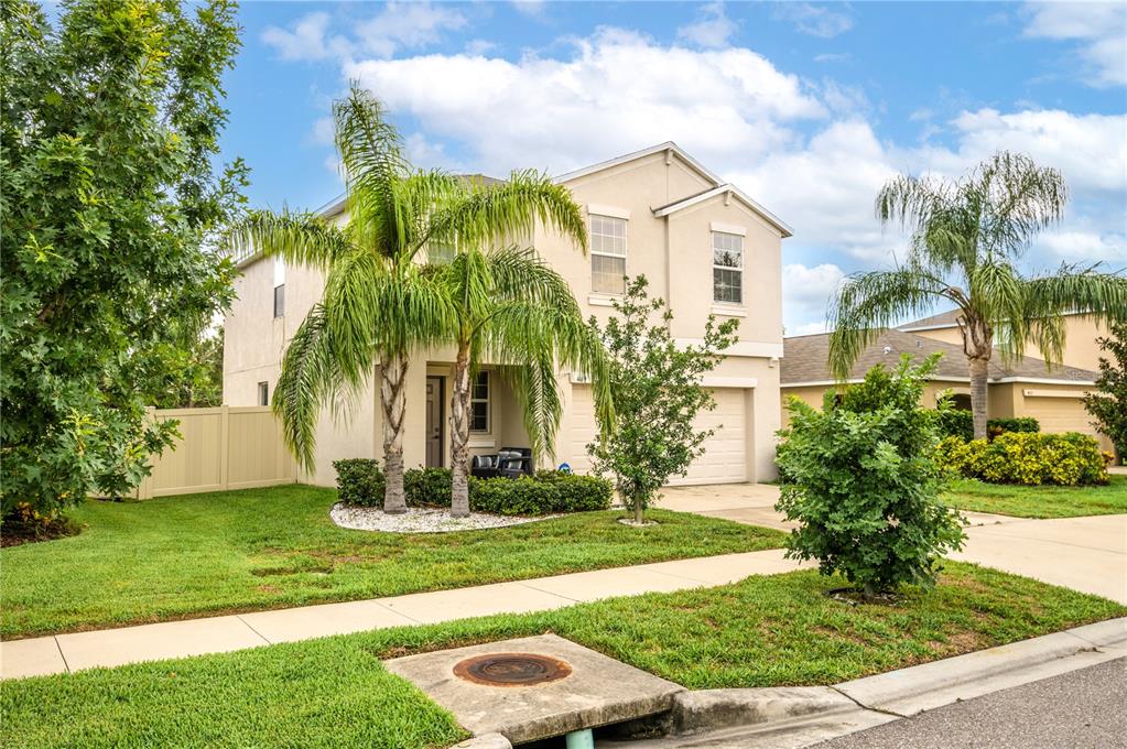 A two-story beige house with a garage, palm trees, and a front lawn — 409 SERENITY MILL LOOP, RUSKIN, FL