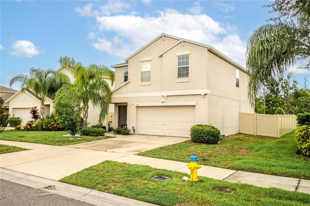 A two-story beige house with a two-car garage and a fire hydrant in the yard — 409 SERENITY MILL LOOP, RUSKIN, FL