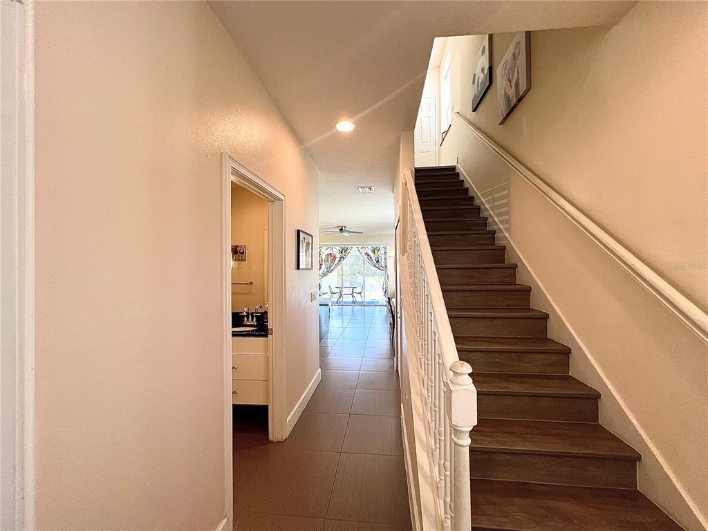 A hallway with tile flooring leads to a living area past a staircase and bathroom — 17407 PLACIDITY AVENUE, CLERMONT, FL