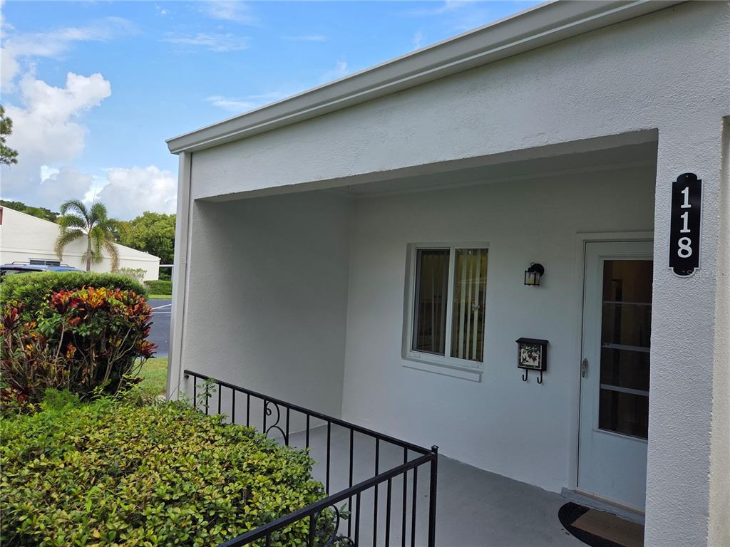 An exterior view of a white building entrance with a covered porch and metal railing — 2060 MARILYN STREET UNIT 118, CLEARWATER, FL
