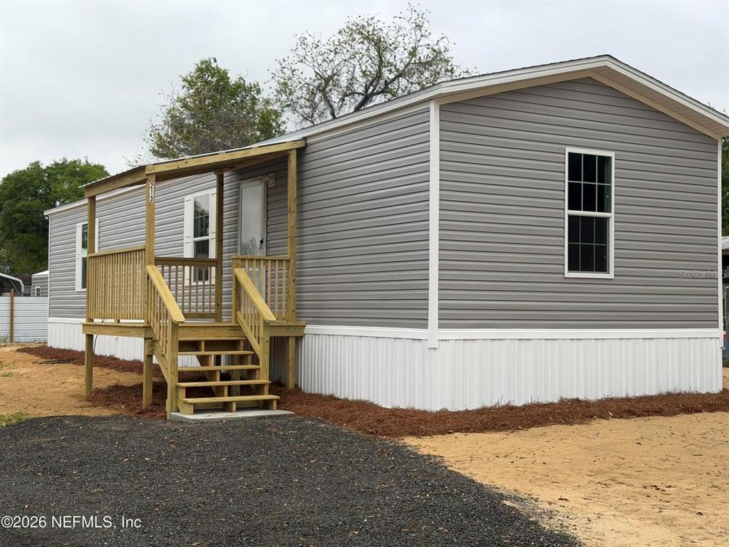 A gray manufactured home features a wooden front deck and stairs on a gravel lot — 213 MILTON AVENUE, INTERLACHEN, FL